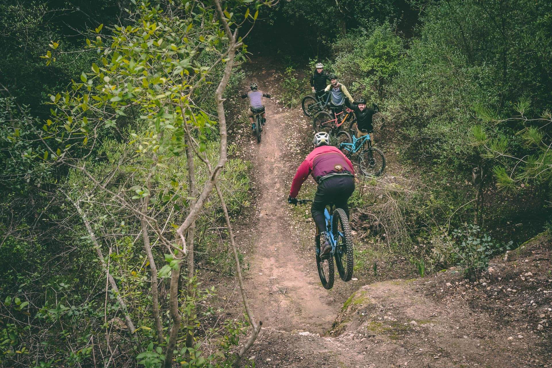 A group of mountain bike riders watching while one of them drops on a technical session during a tour in Monsanto (Portugal)